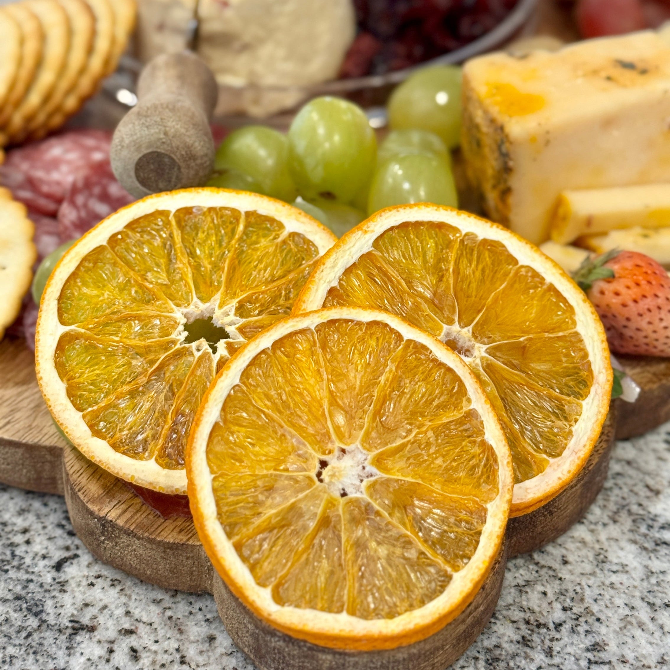 Dried orange slices on a wooden board with a cheese and fruit platter in the background.